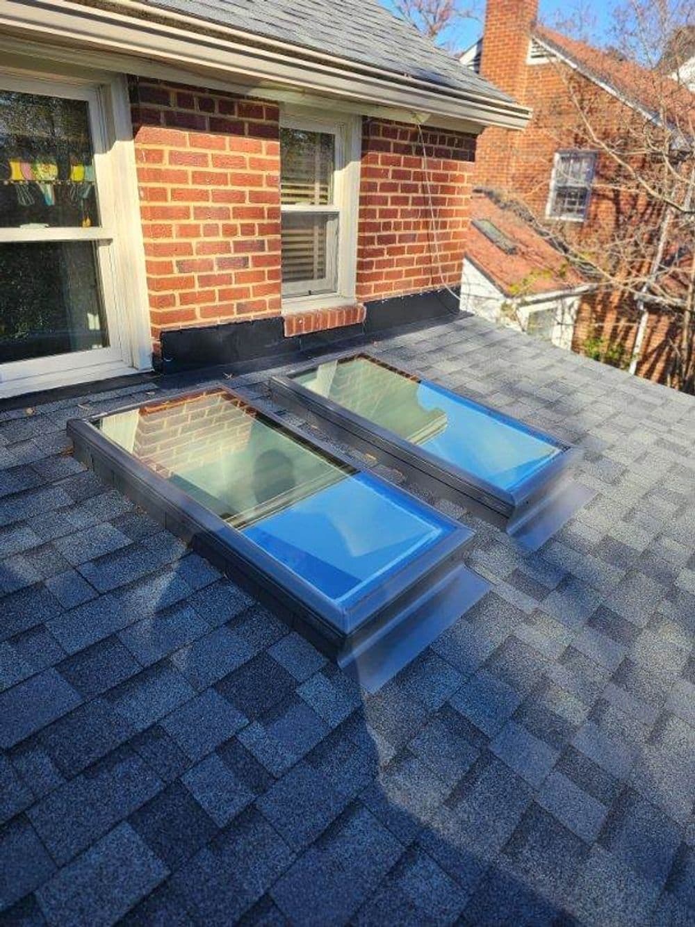 Modern skylights on a residential roof with a brick wall backdrop and sunny atmosphere.