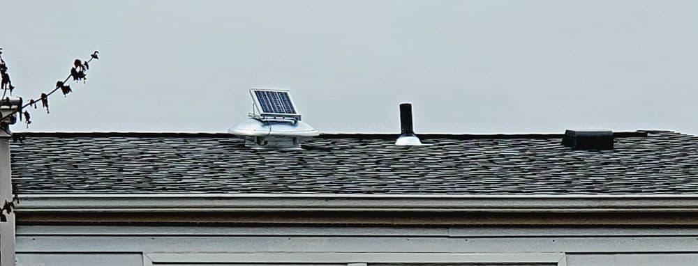 Solar panel and ventilation pipes on a roof under a gray sky.