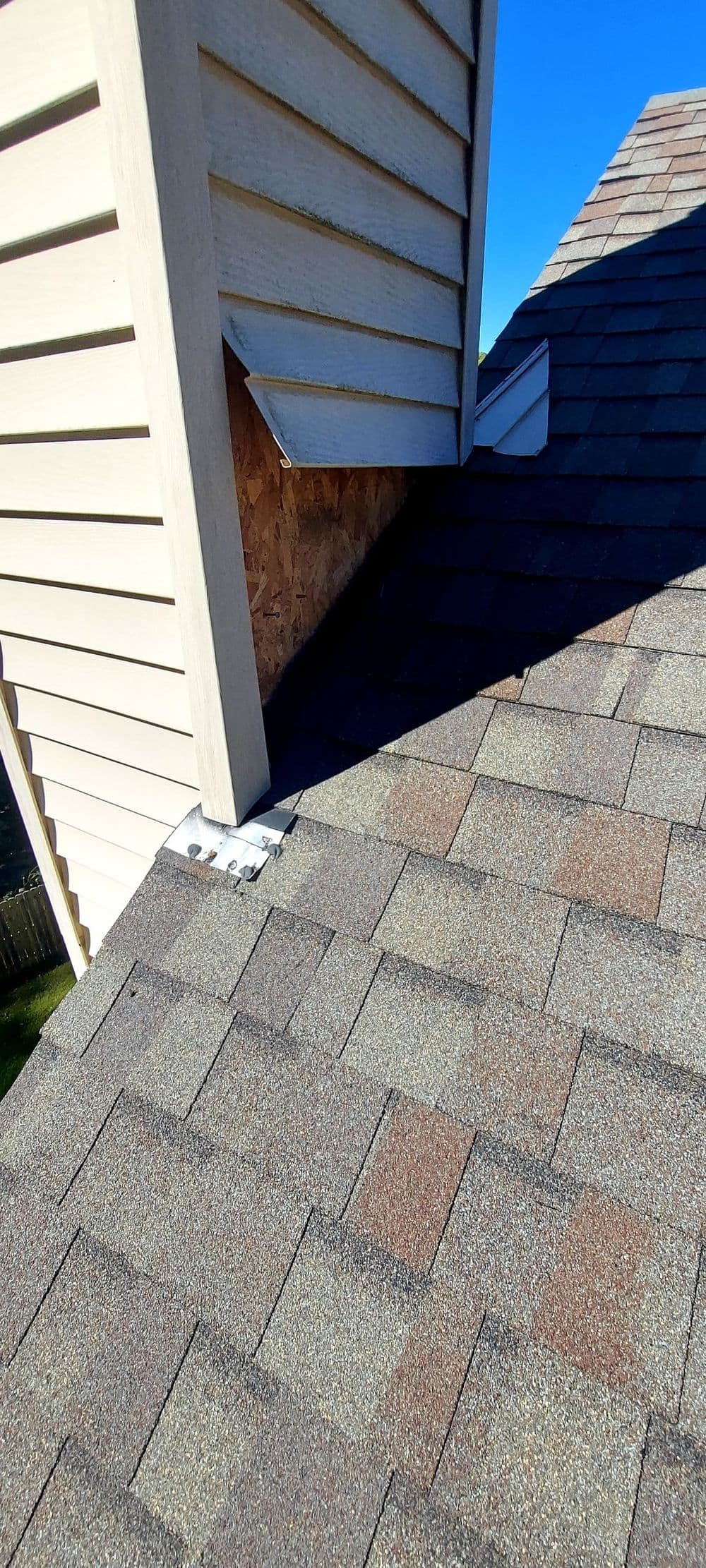 Rooftop view showing shingles and chimney intersection under clear blue sky.