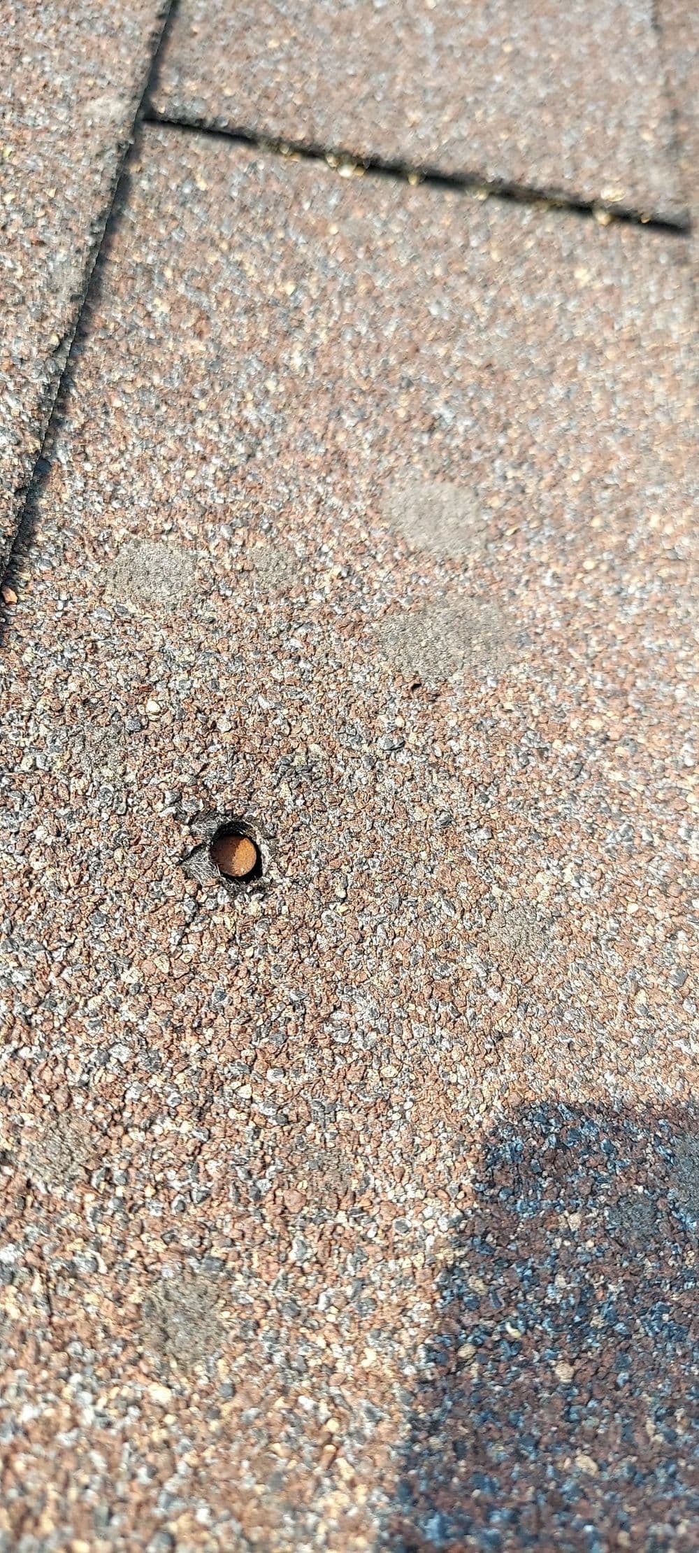 Close-up of a hole in a roof shingle, showing potential water damage risk.