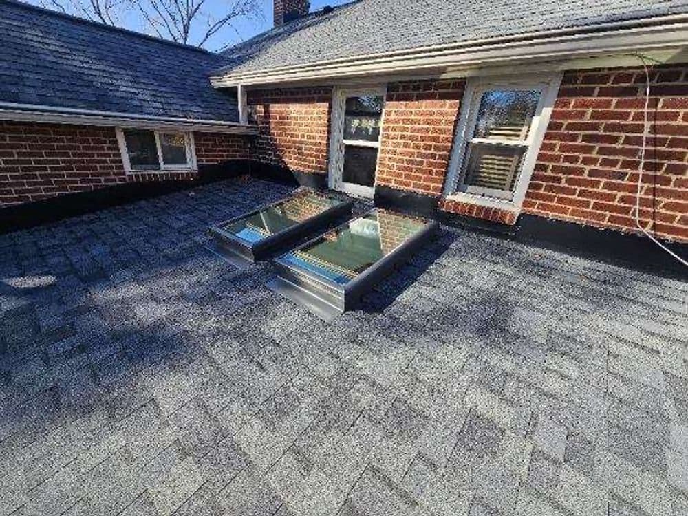 Two skylights on an asphalt shingle roof of a brick house, providing natural light.