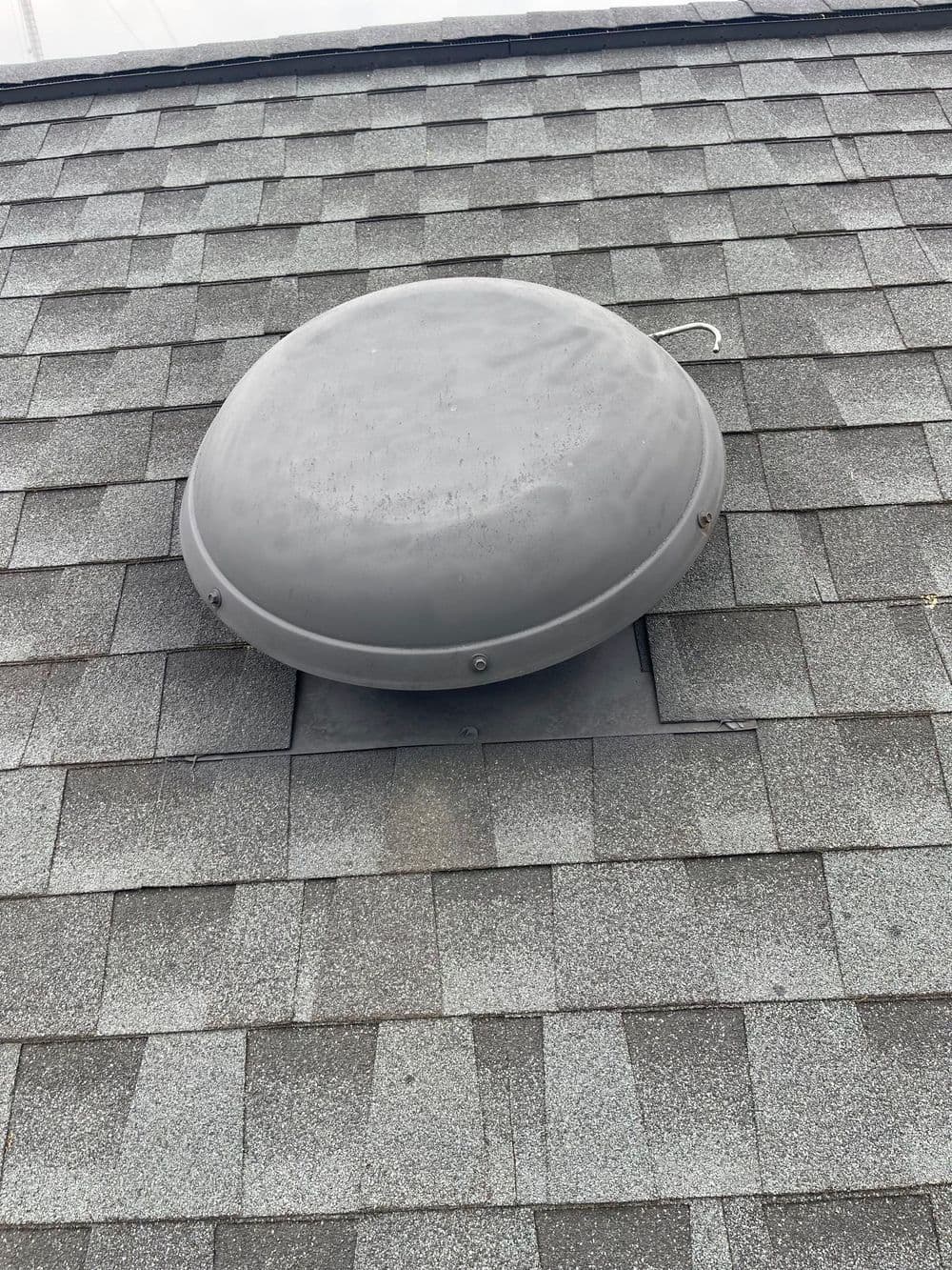 Roof-mounted ventilation dome on shingle rooftop for improved airflow and moisture control.