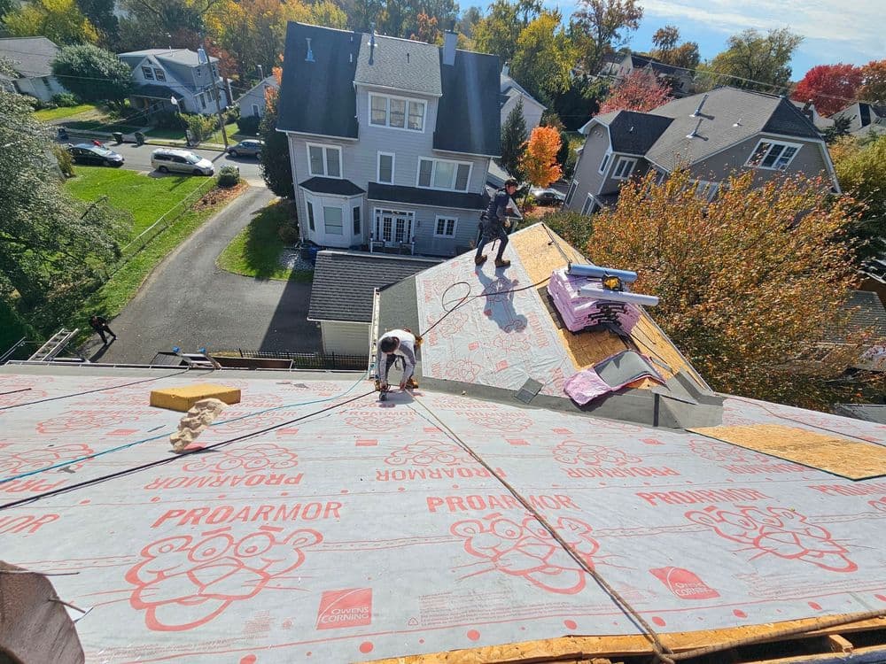 Roofing installation with workers applying ProArmor underlayment on residential home.