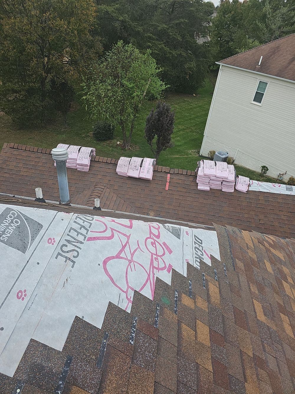 Roofing installation with pink insulation stacks and shingles, viewed from above.