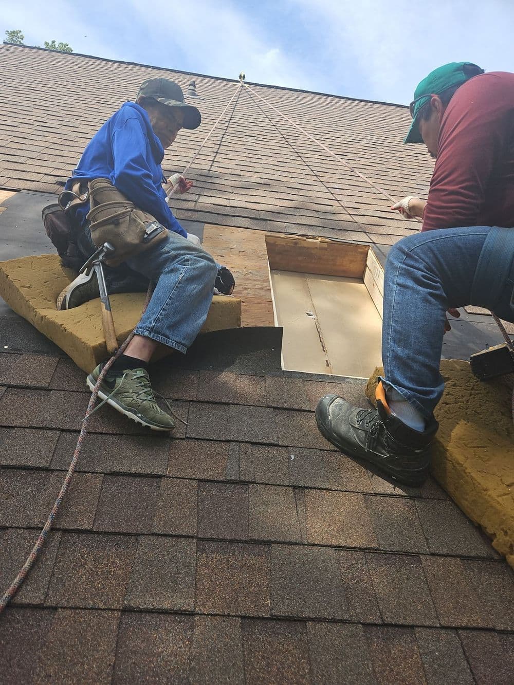 Two roofers working on repairs using safety harnesses on a shingled roof.
