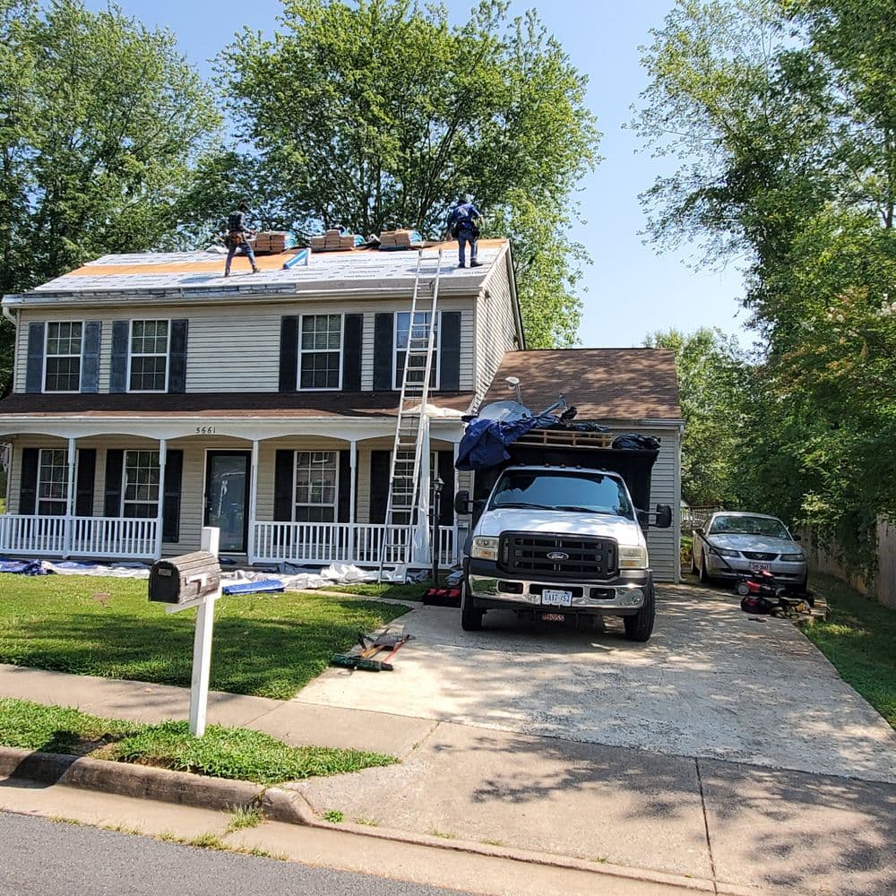 Roof repair in progress on a two-story house with workers and equipment visible.