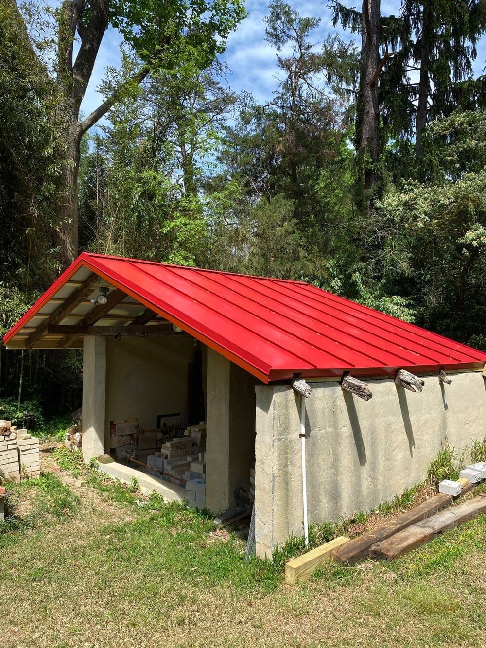Red metal roof on a rustic storage shed surrounded by lush greenery and trees.