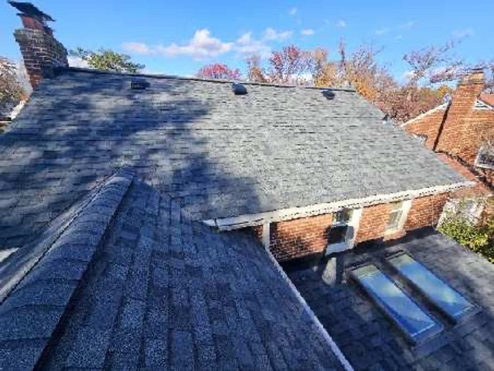 Aerial view of a gray shingle roof with skylights and autumn trees in the background.