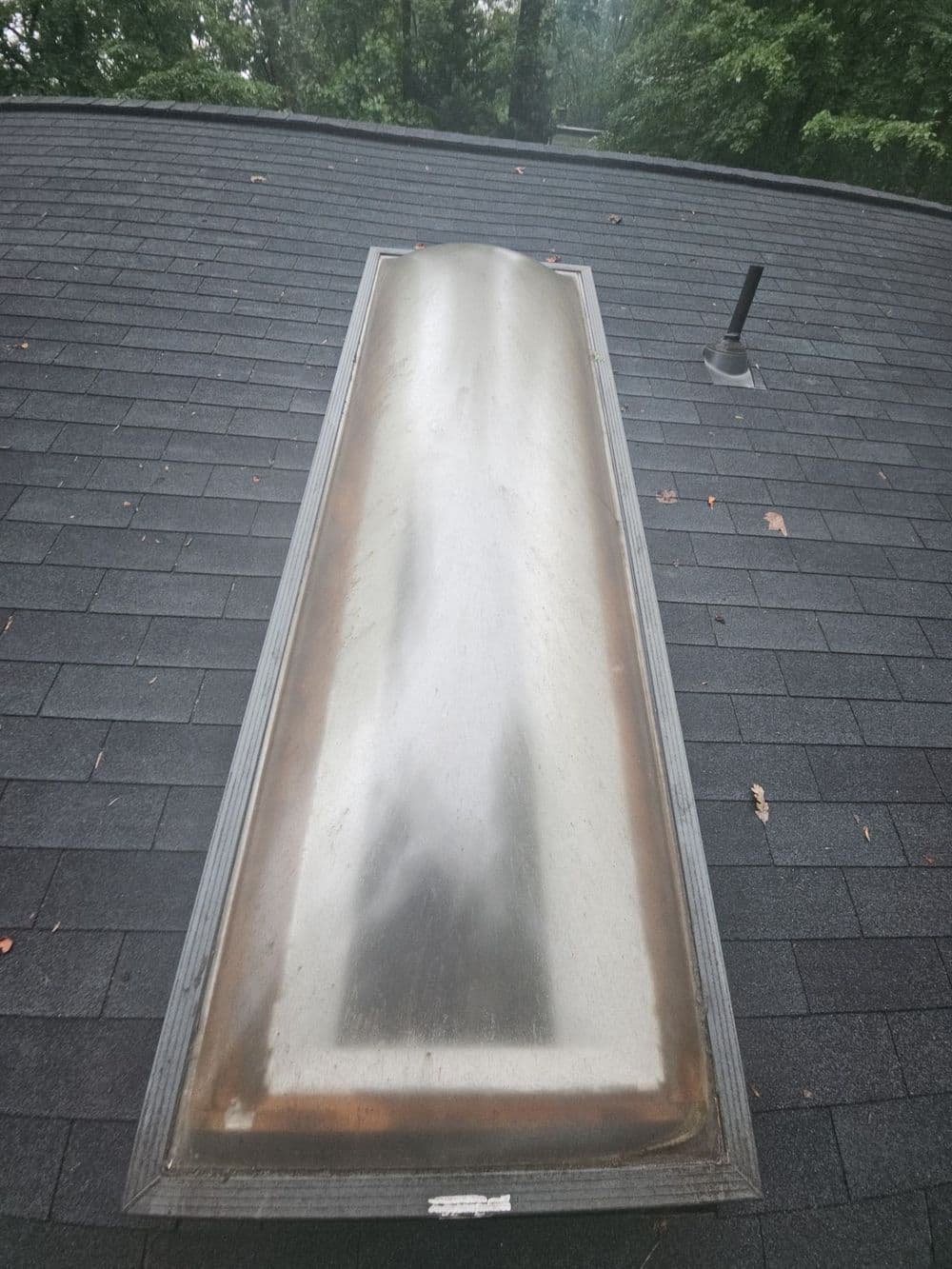 Skylight on a shingled roof showing signs of wear and weathering.