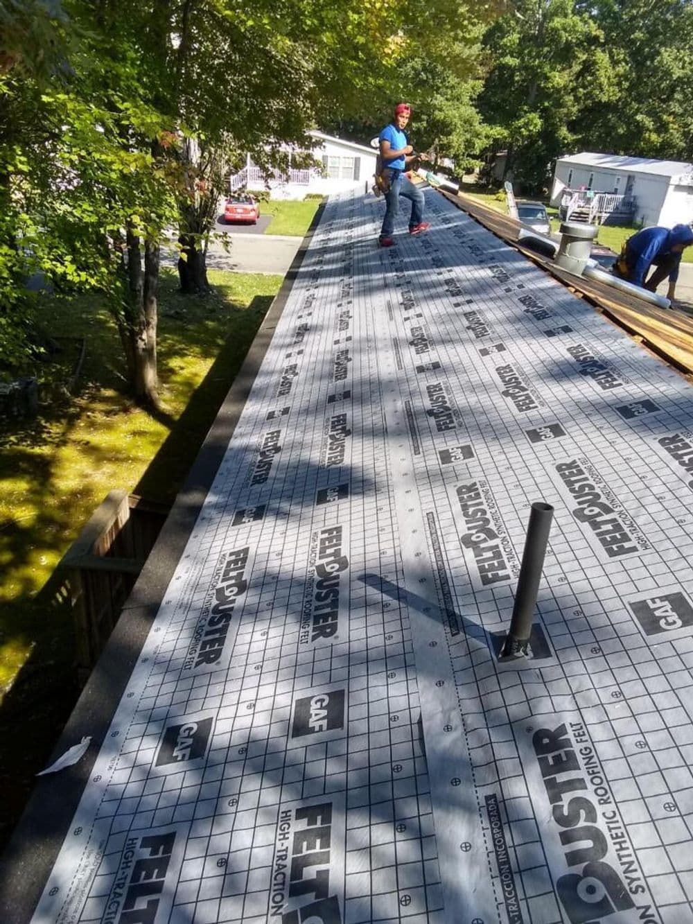 Roofing project in progress with a worker installing synthetic underlayment on a home.