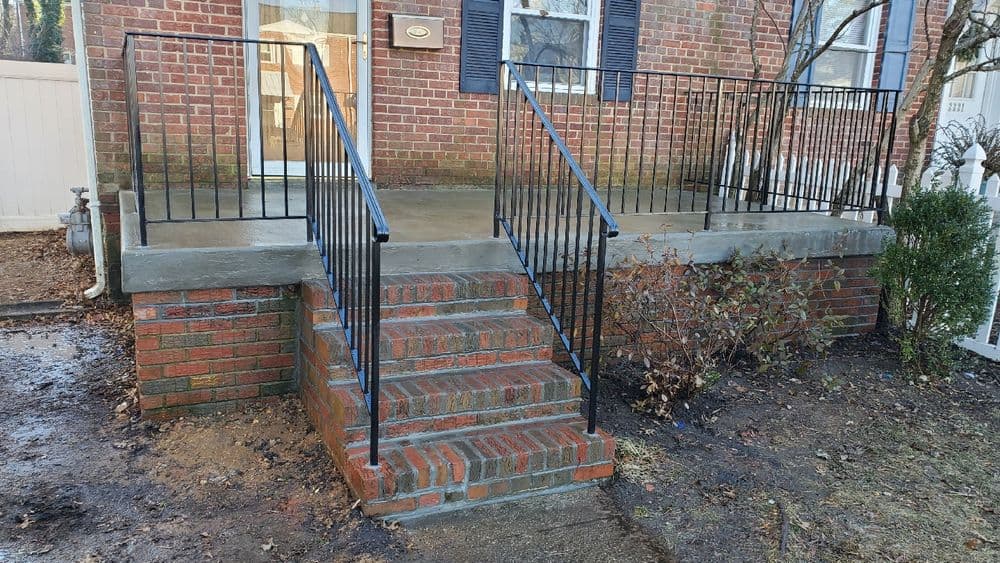 Brick stairs with black railings leading to a brick house entrance and porch.