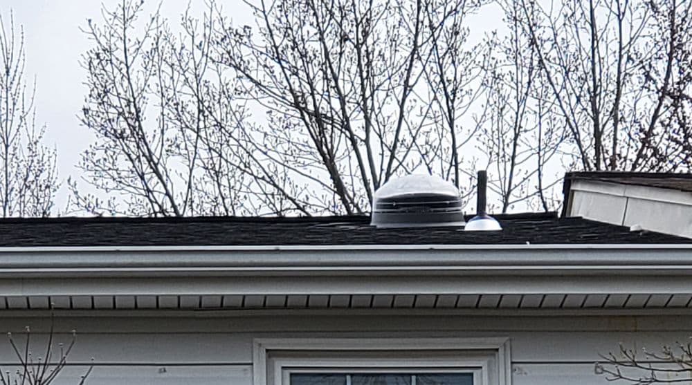 Roof with venting system and snow accumulation, surrounded by leafless trees in winter.