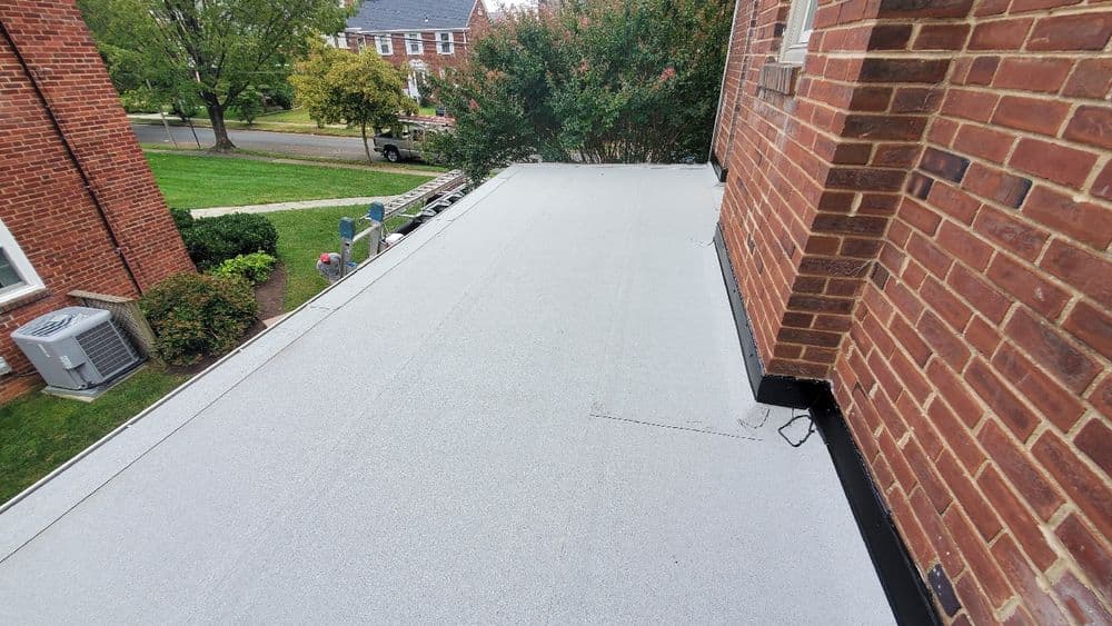 Flat roof installation with gray surface, surrounded by brick buildings and greenery.