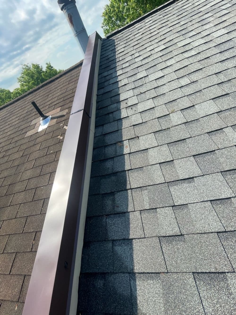 Roof with asphalt shingles, chimney vent, and contrasting shadow along the ridge line.