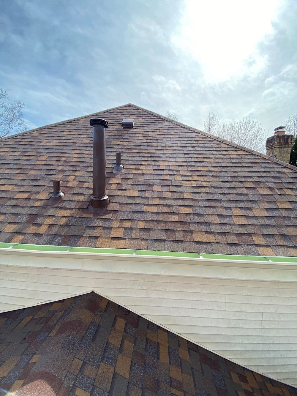 Newly installed asphalt shingle roof with chimney and vents against a cloudy sky.