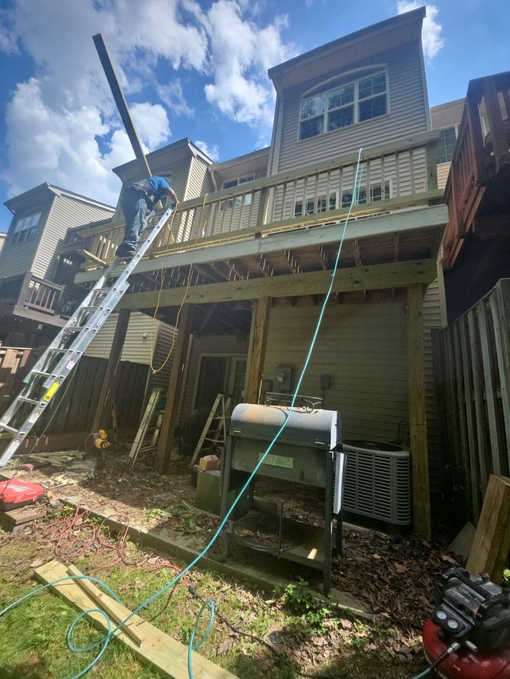 Home renovation project with a ladder, tools, and a deck under construction. Sunny day.