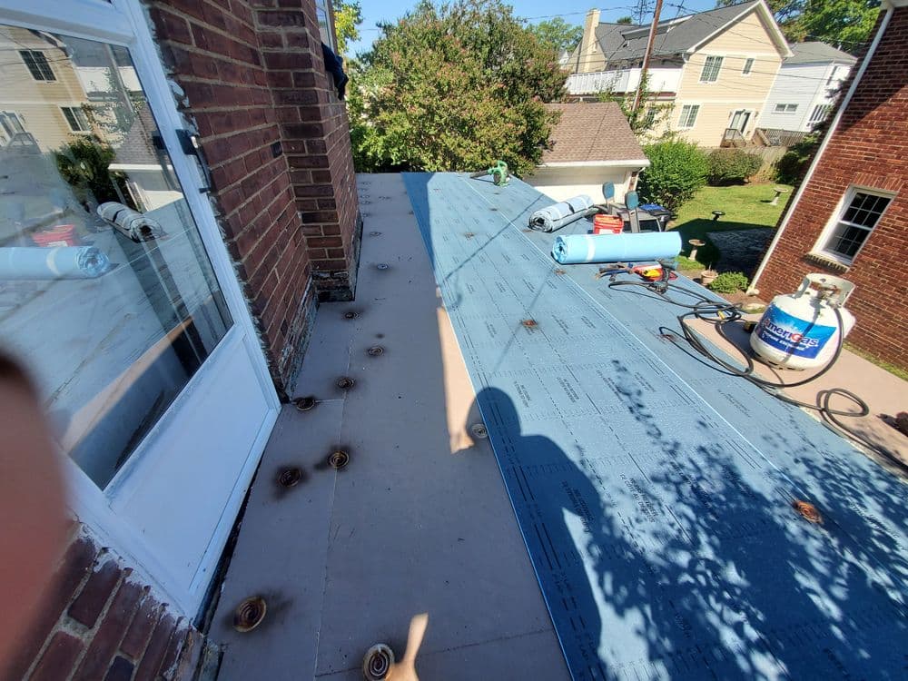 Flat roof installation showing blue underlayment and roofing equipment on a residential home.