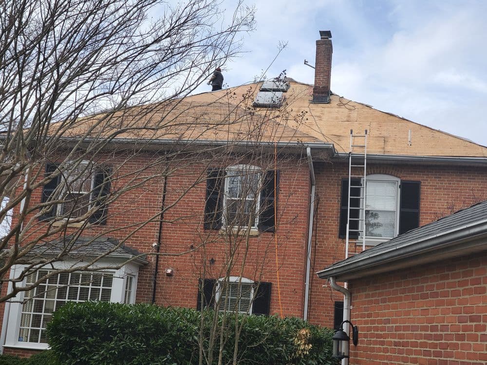 Roofers installing shingles on a residential home with a ladder and skylight visible.