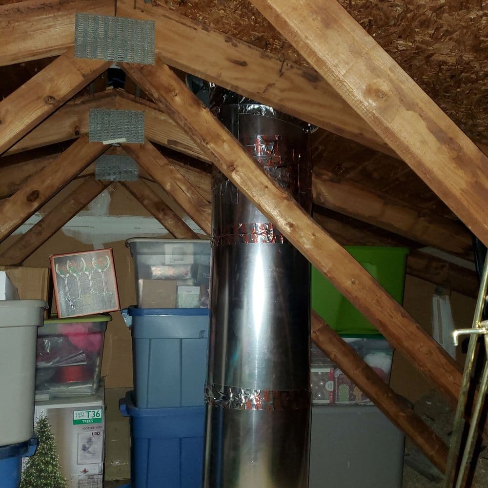 Attic space with storage bins, festive decor, and a metal chimney pipe among wooden beams.