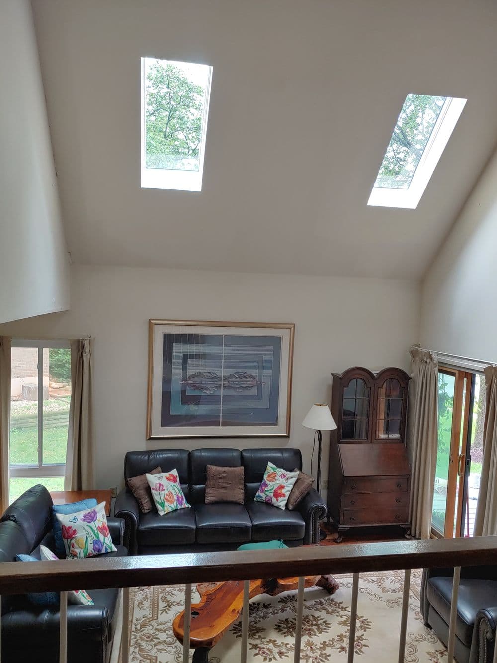 Spacious living room with skylights, black leather sofa, and colorful throw pillows.