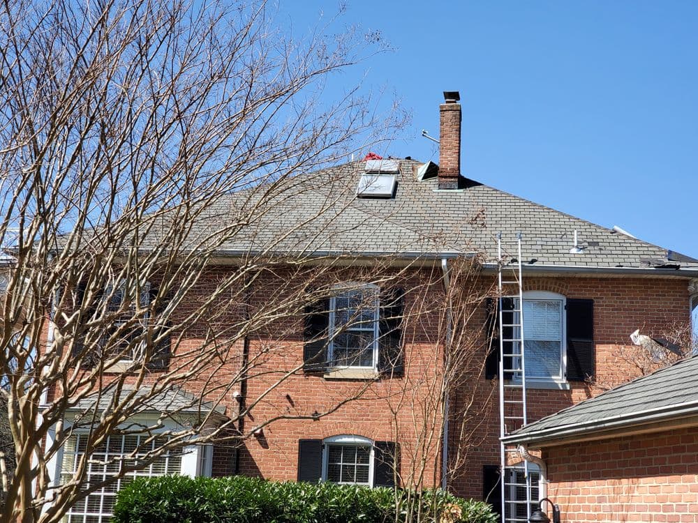 Residential roof repair with ladder and chimney under clear blue sky.