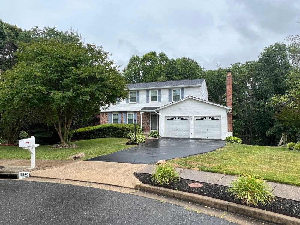 Two-story white house with brick accents, green lawn, and paved driveway on a quiet street.