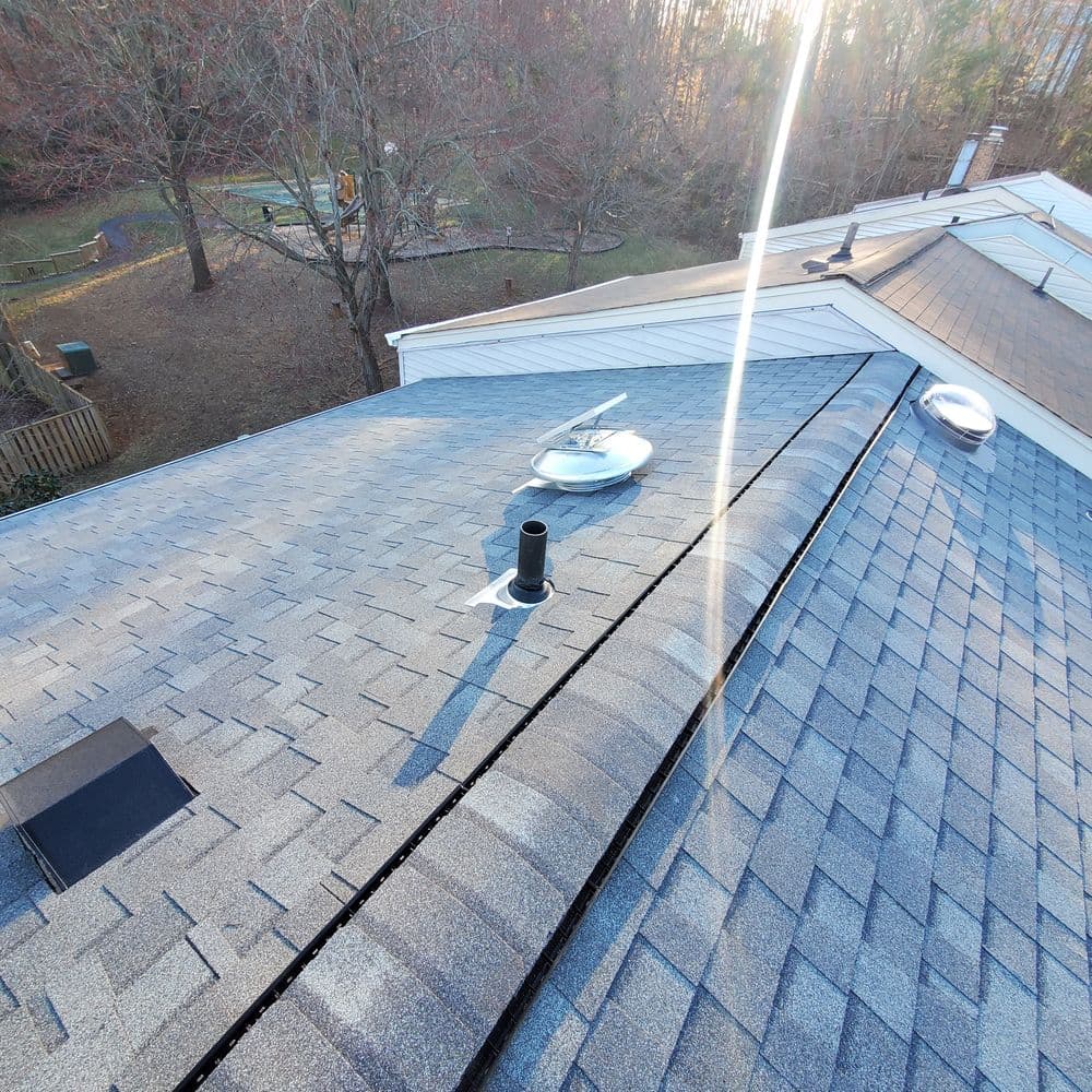 Aerial view of a gray shingle roof with vents and sunlight glinting off the surface.