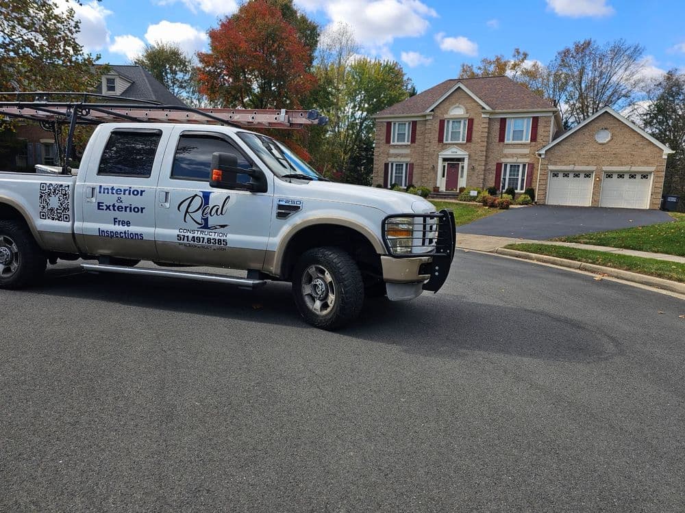 White pickup truck with a ladder on top parked in front of a well-maintained house.