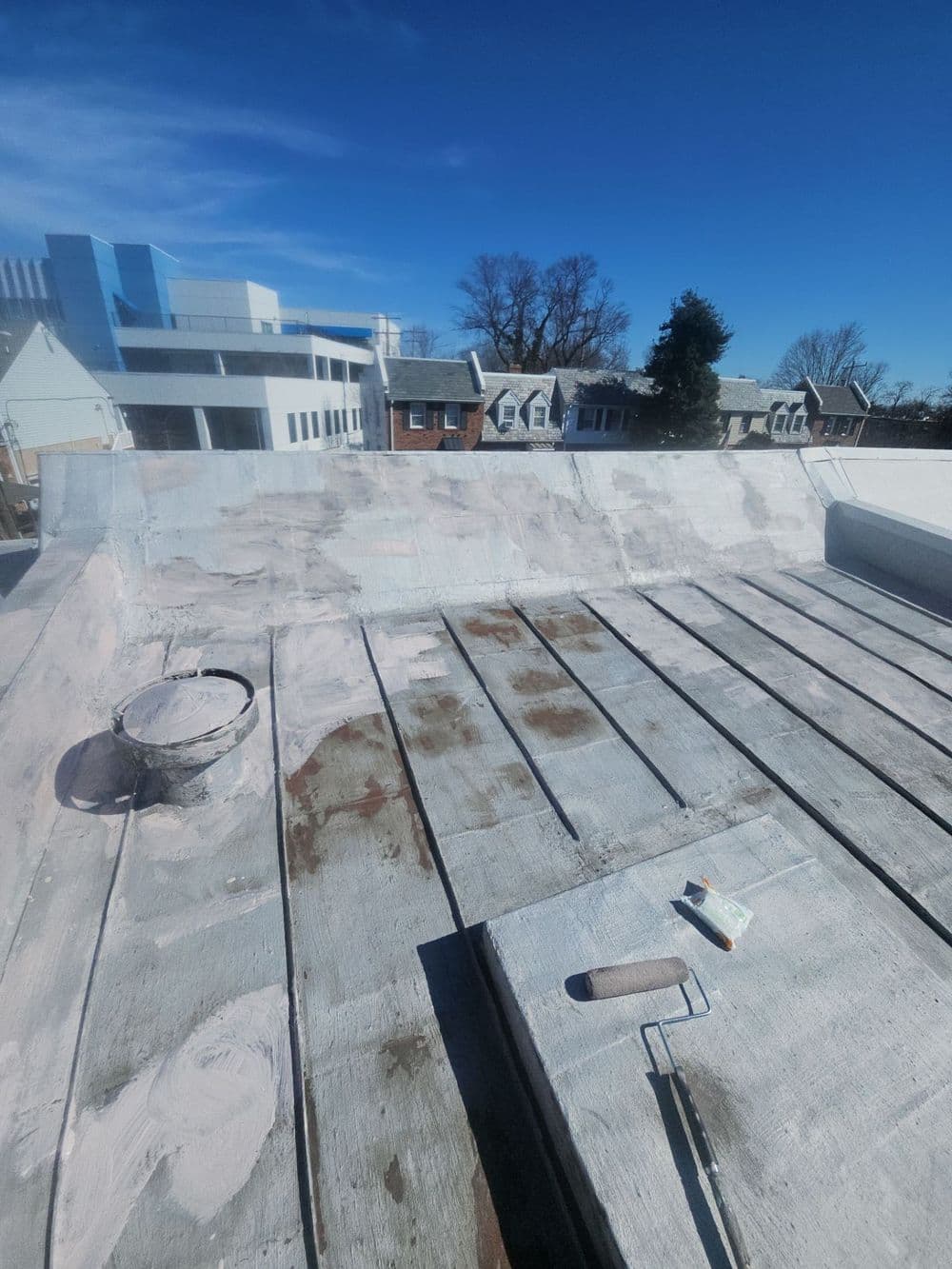 Freshly coated flat roof with painting supplies and blue sky backdrop.