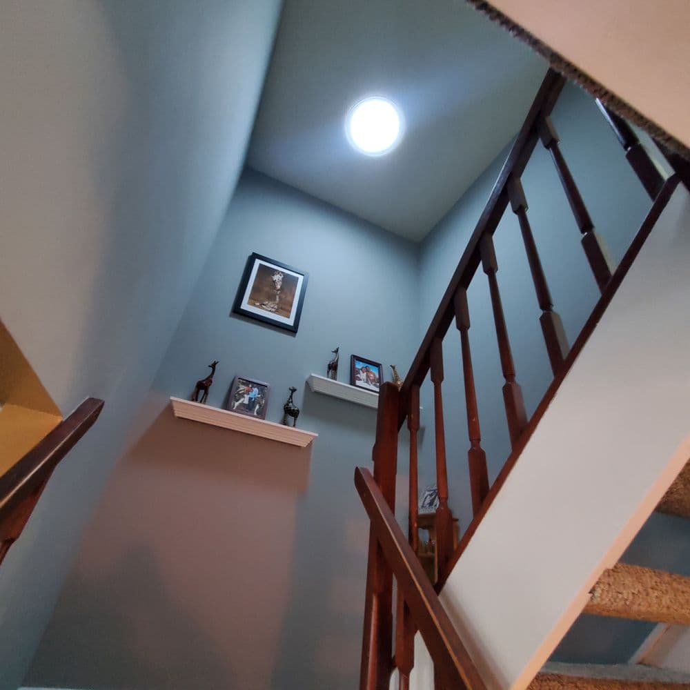 View of a staircase leading to a bright skylight, framed artwork, and wooden railing.