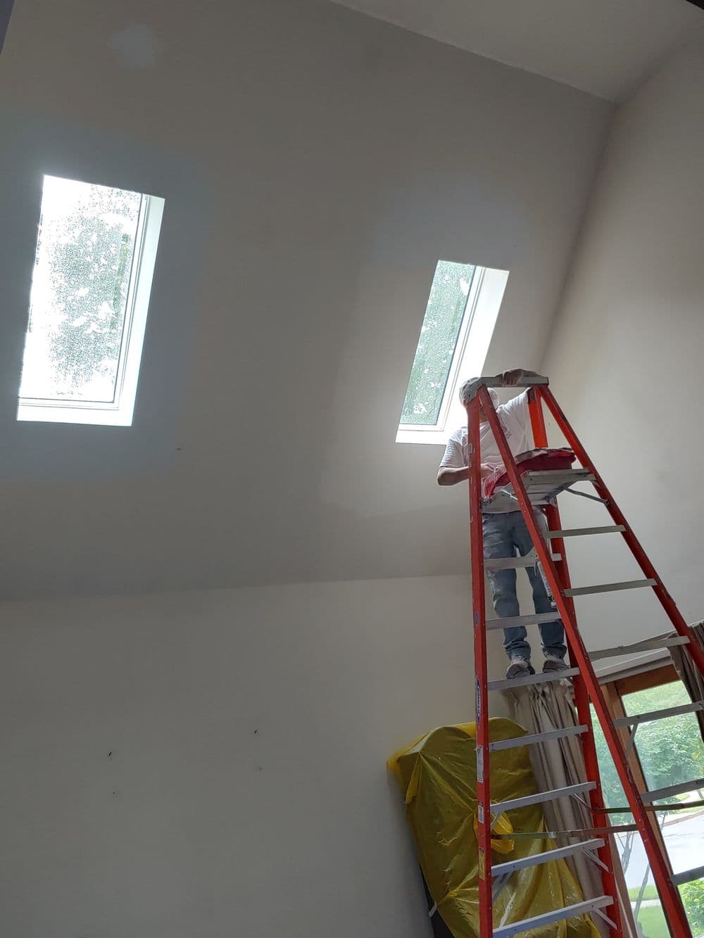 Worker on ladder installing skylights in a modern room with sloped ceiling.