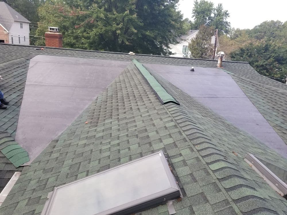 Newly installed black roofing material on a green shingle roof with skylights.