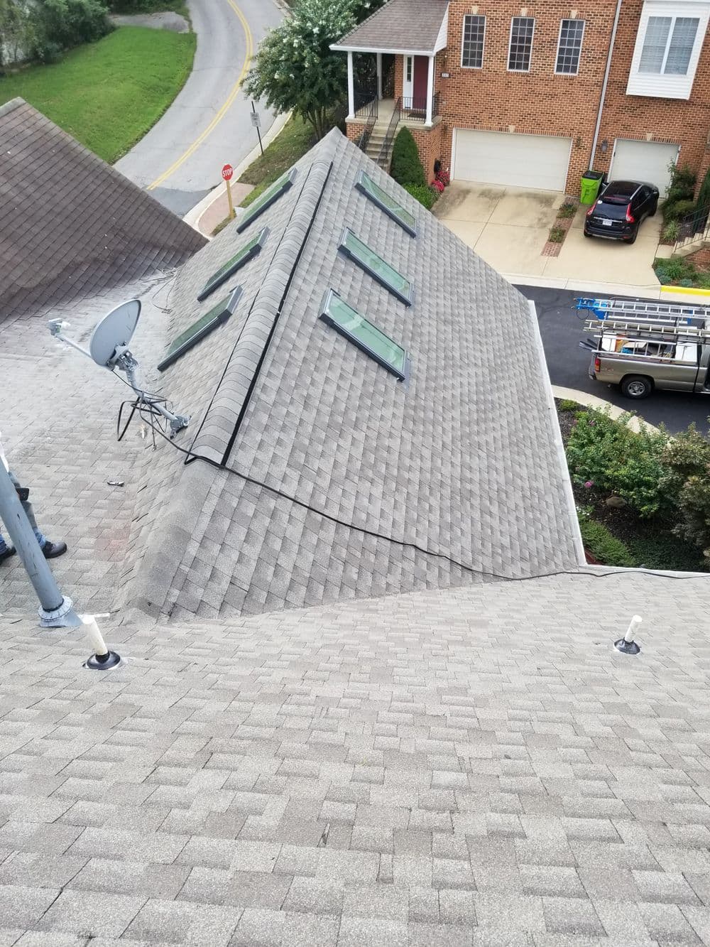 Roof with skylights and satellite dish, showcasing textured shingles and residential setting.
