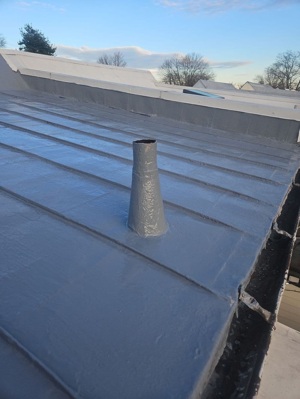 Vent pipe on a gray metal roof under a clear sky. Proper ventilation for roofing systems.